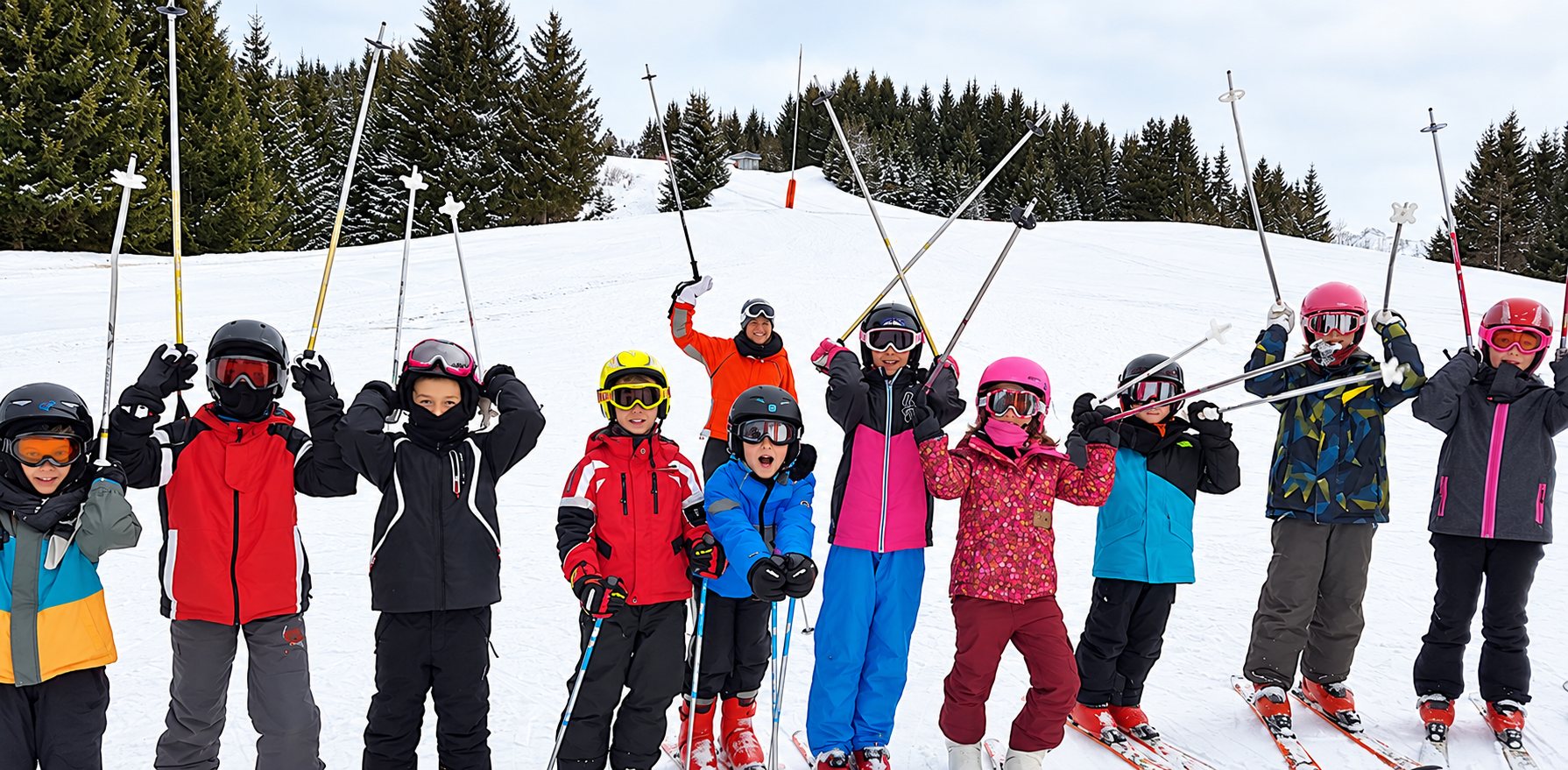 Un groupe d’enfants casqués et équipés de skis lève ses bâtons en souriant sur une piste enneigée, avec un moniteur en orange derrière eux et des sapins en arrière-plan.